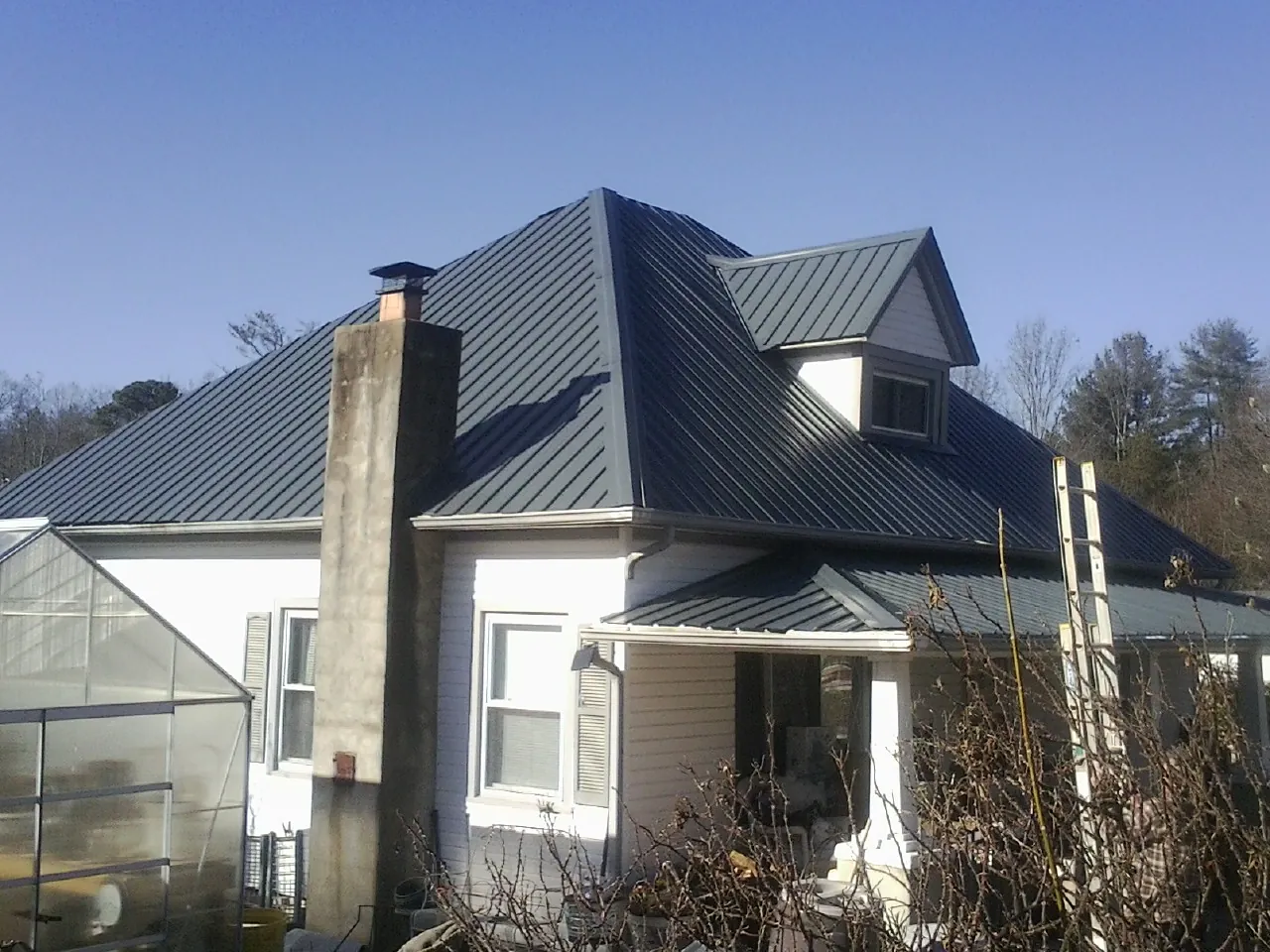 Dark blue standing seam metal roof on a white farmhouse with dormer — Slate & Tile Roof Repair by Roofing Brothers in Knights Landing