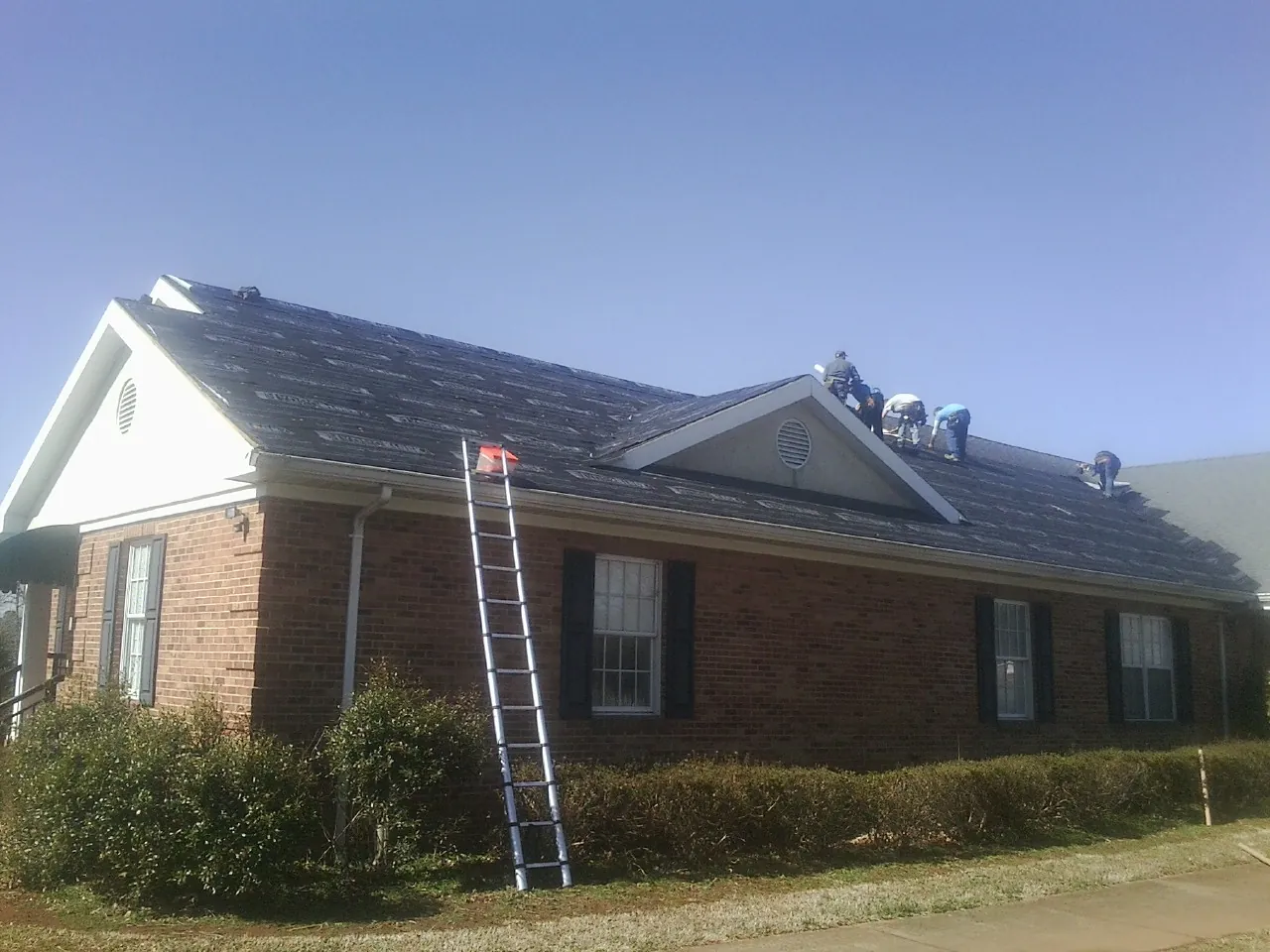Crew tearing shingles off a brick ranch roof with a ladder set — Emergency Roof Repair work by our crew in Knights Landing