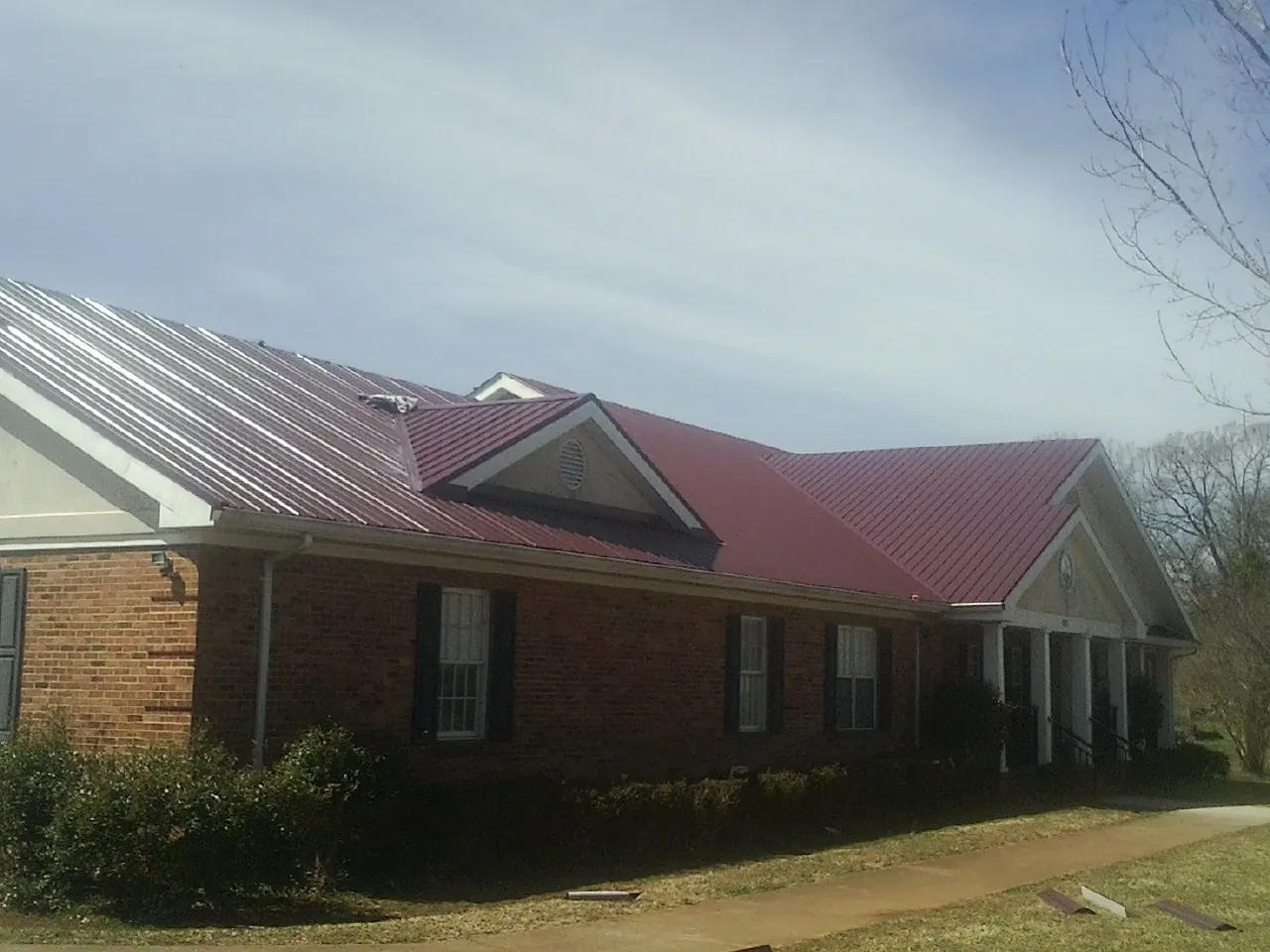 Red metal roof with gabled entries on a long brick building, from a Hail Damage Roof Repair job in Knights Landing