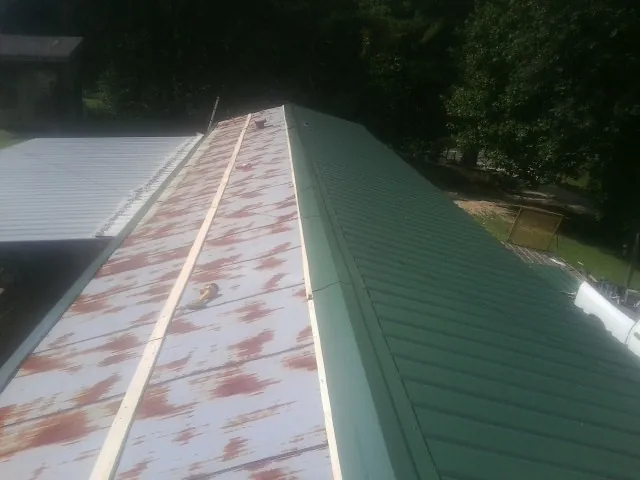 Old rusted panels beside newly installed green metal roofing — Wind Damage Roof Repair by Roofing Brothers in Knights Landing