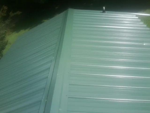 New green metal panels meeting at the ridge of a roof — Flat Roof Repair work by our crew in Knights Landing
