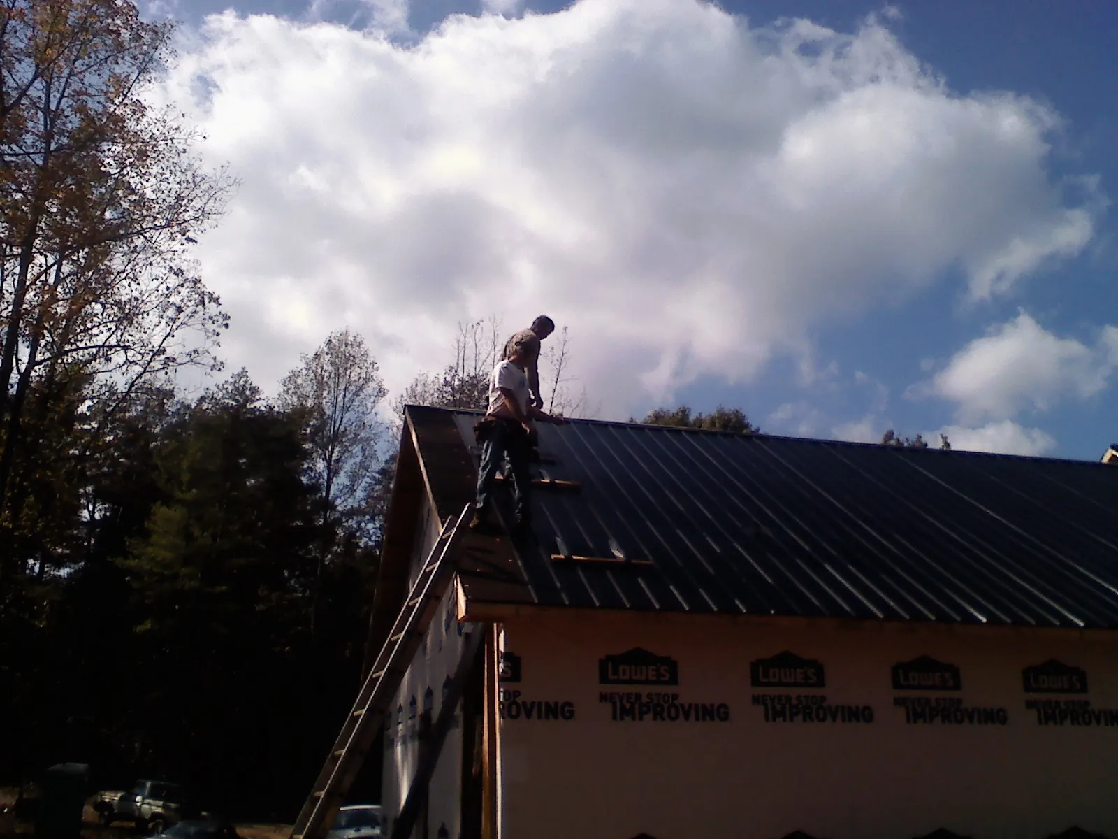 Roofer fastening dark metal panels high against a cloudy sky, from a Roof Inspection job in Knights Landing