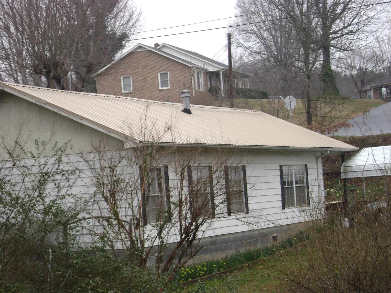 Tan metal roof on a white sided house set into a hillside — Commercial Roofing by Roofing Brothers in Knights Landing